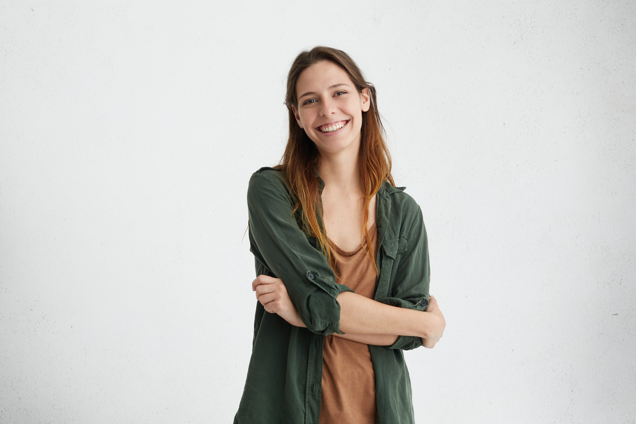 Photo of restful woman with dyed hair standing crossed hands having sincere and delightful smile demonstrating her perfect teeth posing over white studio wall. Happy female rejoicing her life qui som